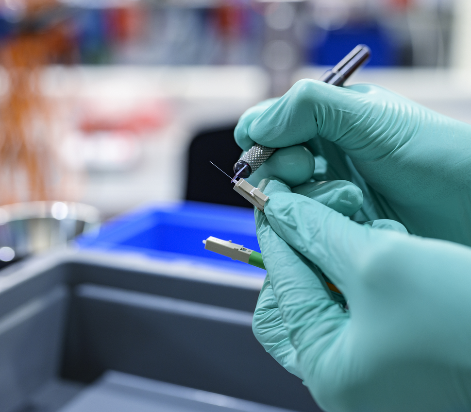 Employee trimming excess fiber from a secured LC connector with a scalpel.