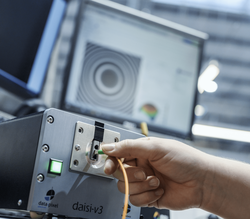 Close-up of a hand inserting a fiber optic cable into an interferometer for radius, apex, and undercut testing, with green light.
